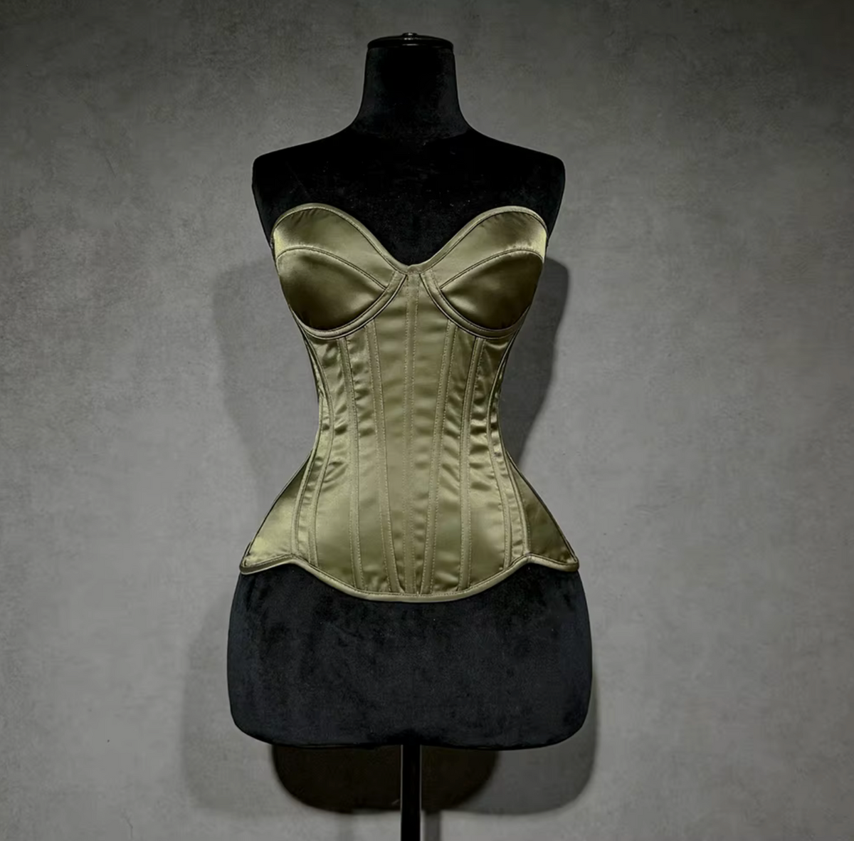 Olive green satin overbust corset with structured cups and steel boning on a black mannequin display.