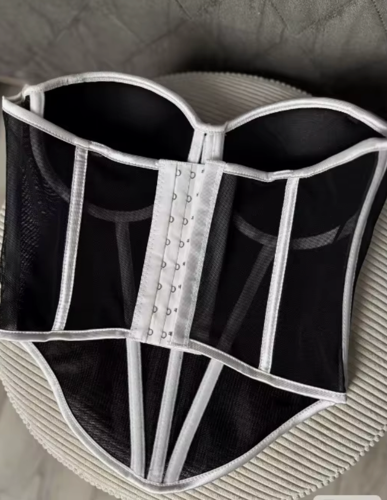 Black mesh corset bustier with white structured piping and a front hook-and-eye closure.