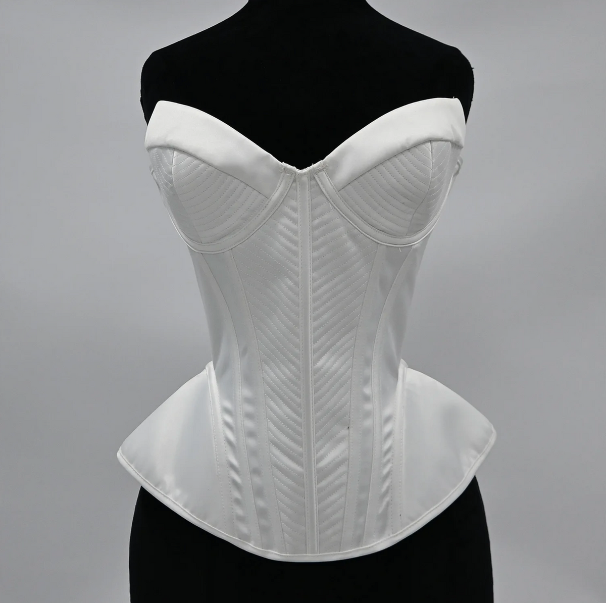 White structured corset bustier with sweetheart neckline, intricate chevron stitching, and a flared peplum waist.