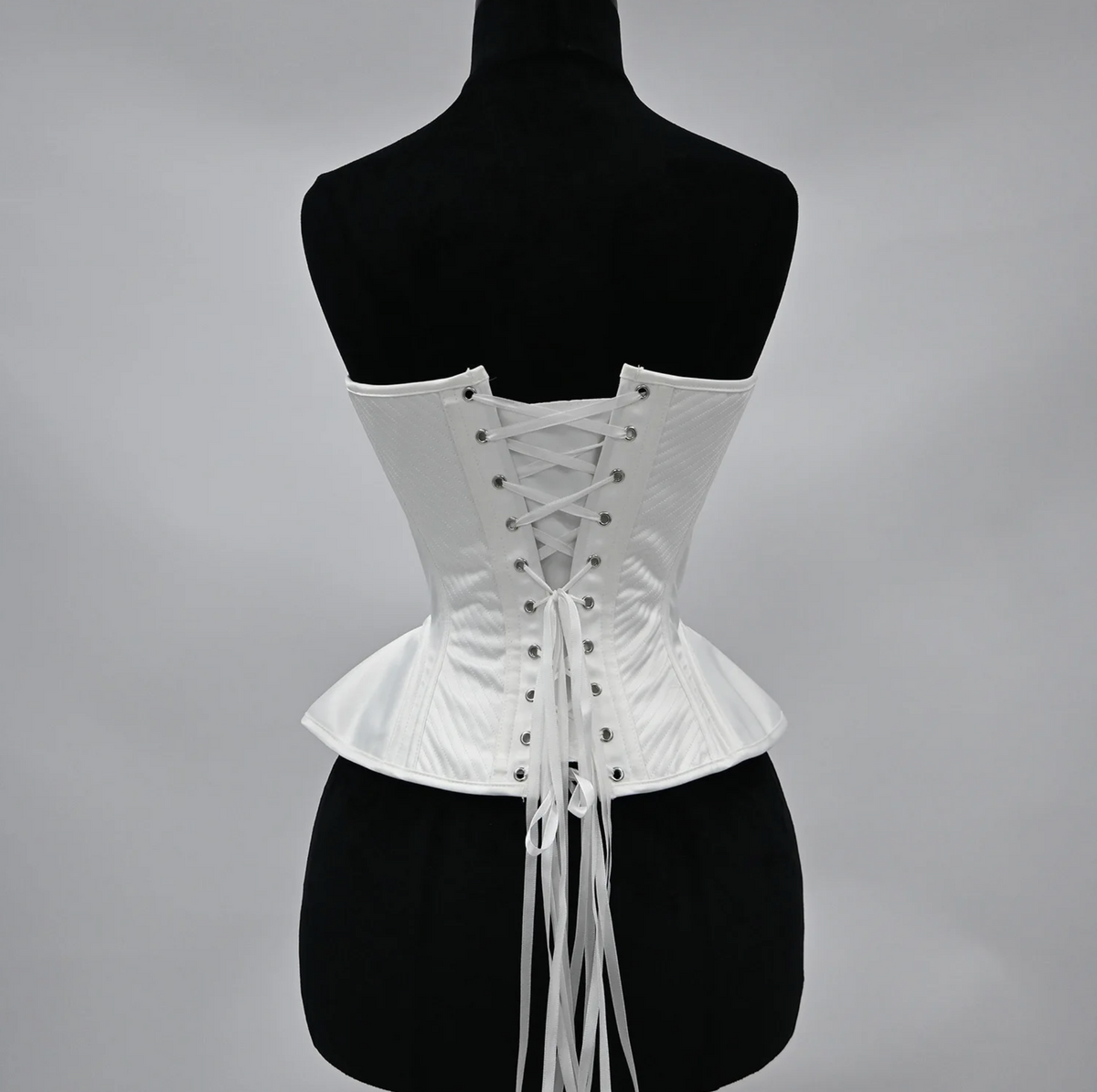 White structured corset bustier with a lace-up back closure and elegant quilted detailing on a black mannequin.