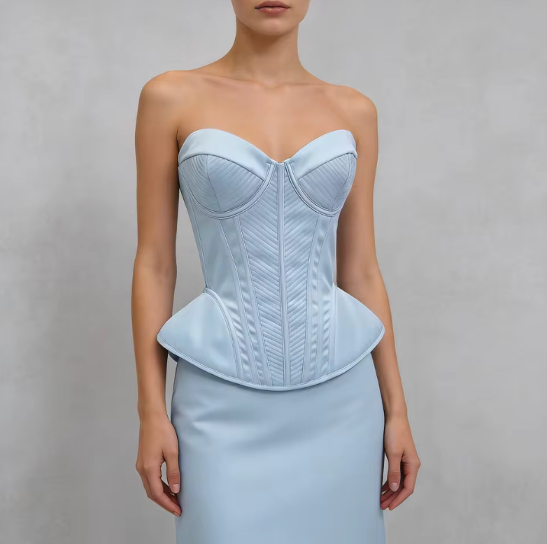 Light blue structured corset bustier with quilted paneling and a peplum waist, worn over a matching skirt.