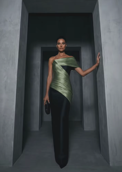 Model wearing a structured olive green and black satin twill floor-length gown with an elegant one-shoulder bodice.