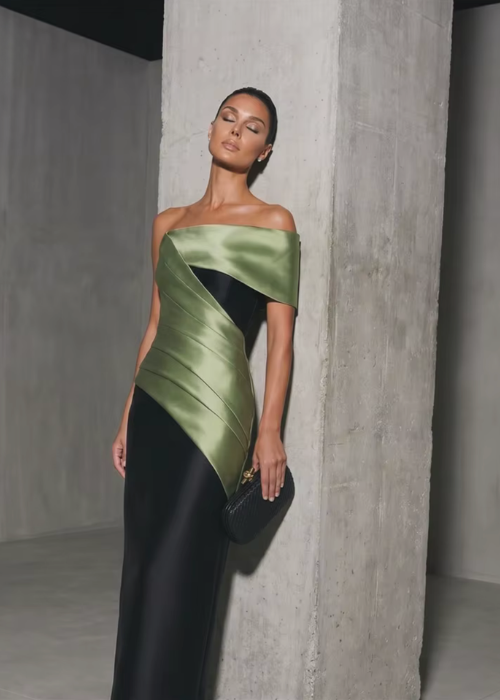 Model wearing a structured off-the-shoulder satin twill gown in olive green and black with a sleek floor-length silhouette.