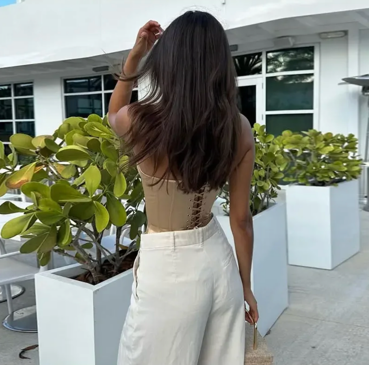 Beige strapless corset top with a lace-up back, worn with cream trousers in an outdoor setting.