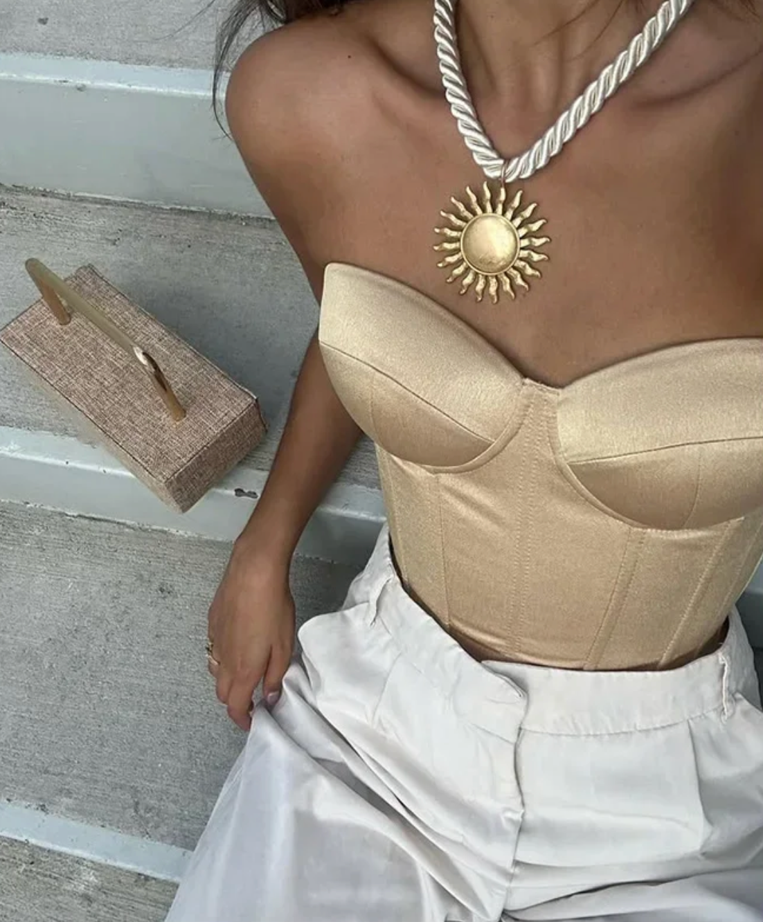 Sleek gold strapless bandage corset top with a structured, cropped silhouette paired with white trousers.