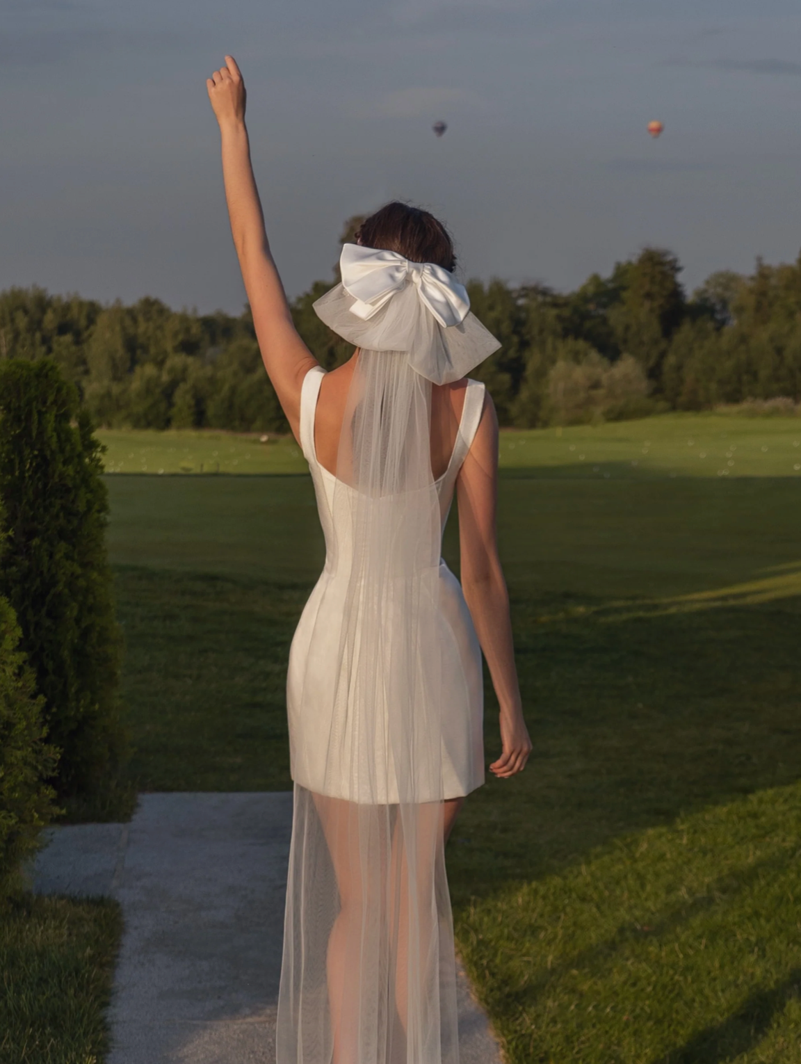 White structured bridal mini dress with corset bodice, square neckline, and sheer veil with a large satin bow.