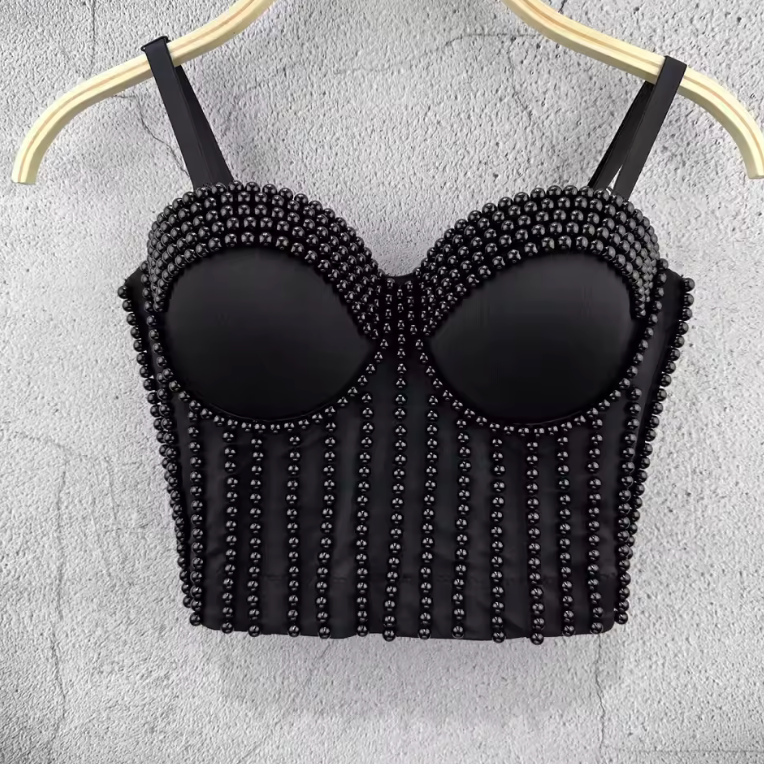 Black corset camisole featuring vertical beaded embellishments and molded cups, hanging on a hanger against a grey wall.