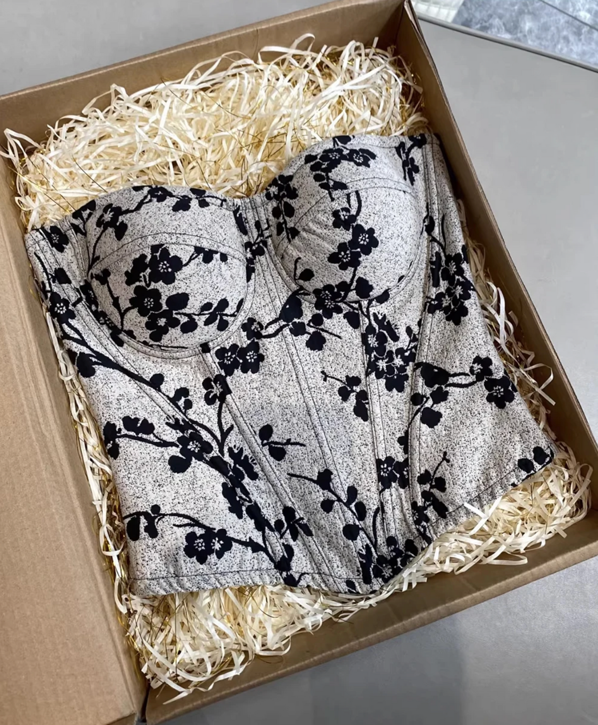 Ivy bustier corset with black floral print on a textured grey background, featuring structured cups in a gift box.