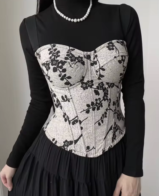 Ivy bustier corset in cream with black floral print, featuring structured cups and steel boning over a black long-sleeve top.