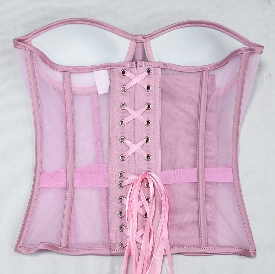 The Lilah light pink sheer mesh corset with a lace-up back closure, featuring multiple adjustable laces, silver metal eyelets, and a matching pink waistband, laid flat against a white background.