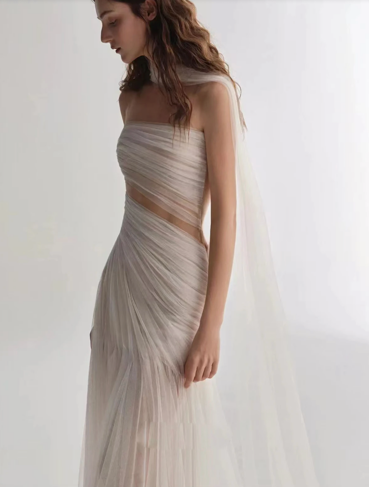 A woman wearing the Old Money Collection La Digue Gown with a sheer neck and pleated tulle, featuring a long ribbon.