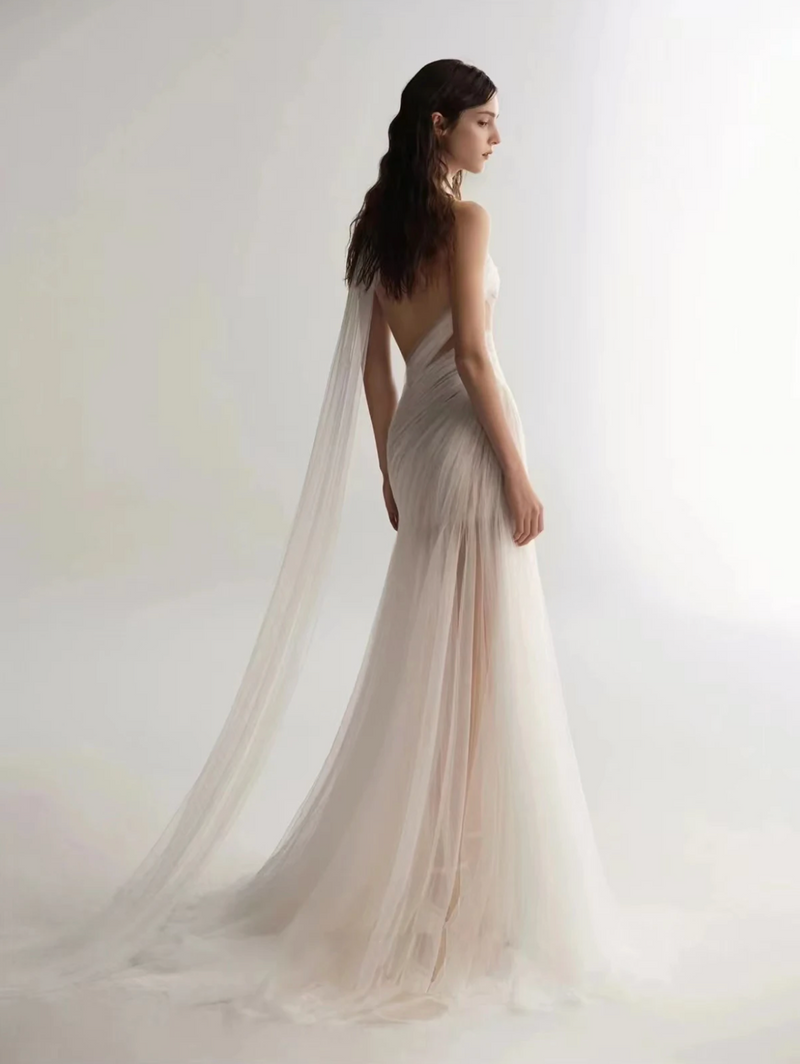 A woman wearing the Old Money Collection La Digue Gown with a sheer neck and pleated tulle, featuring a long ribbon.
