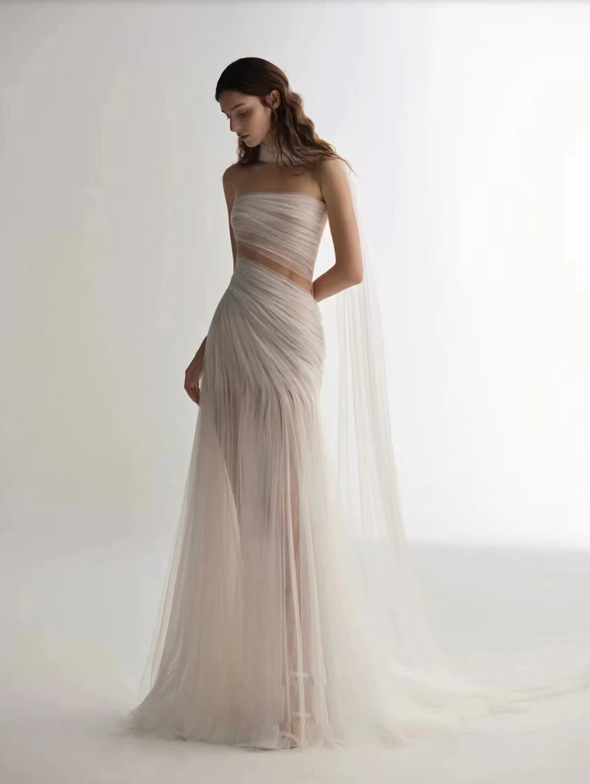 A woman wearing the Old Money Collection La Digue Gown with a sheer neck and pleated tulle, featuring a long ribbon.