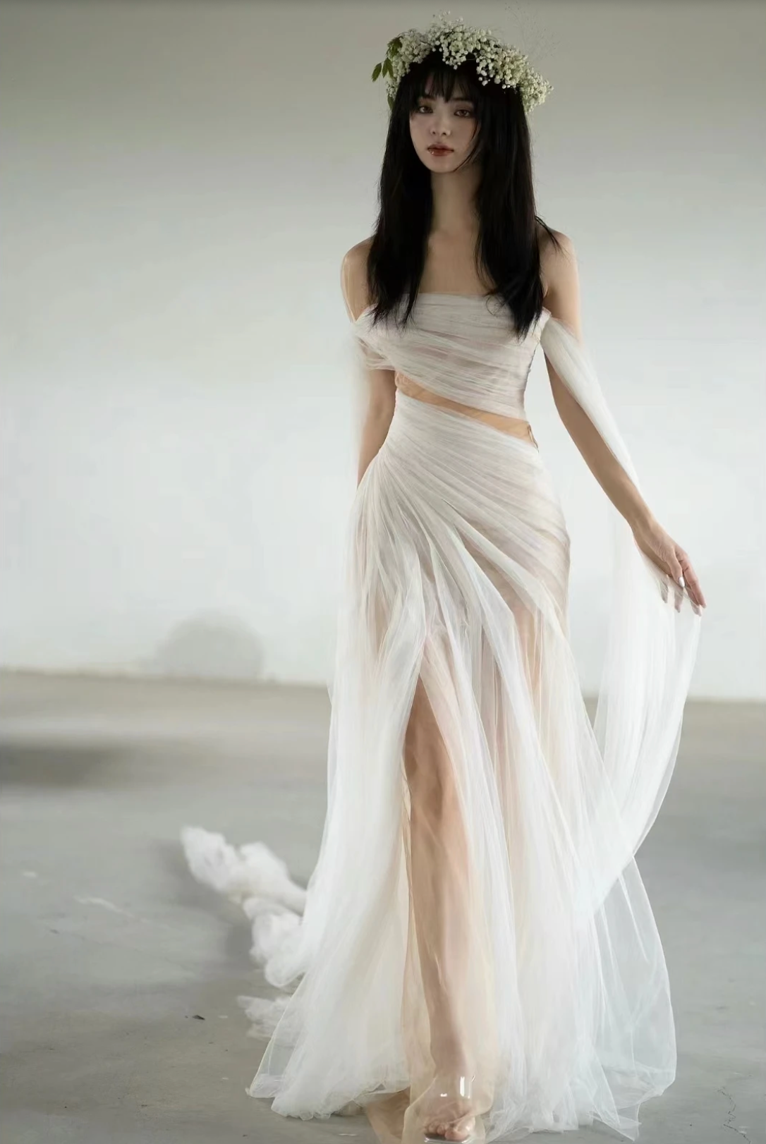 A woman wearing the Old Money Collection La Digue Gown with a sheer neck and pleated tulle, featuring a long ribbon.