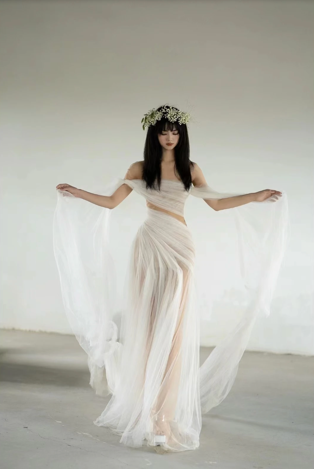 A woman wearing the Old Money Collection La Digue Gown with a sheer neck and pleated tulle, featuring a long ribbon.