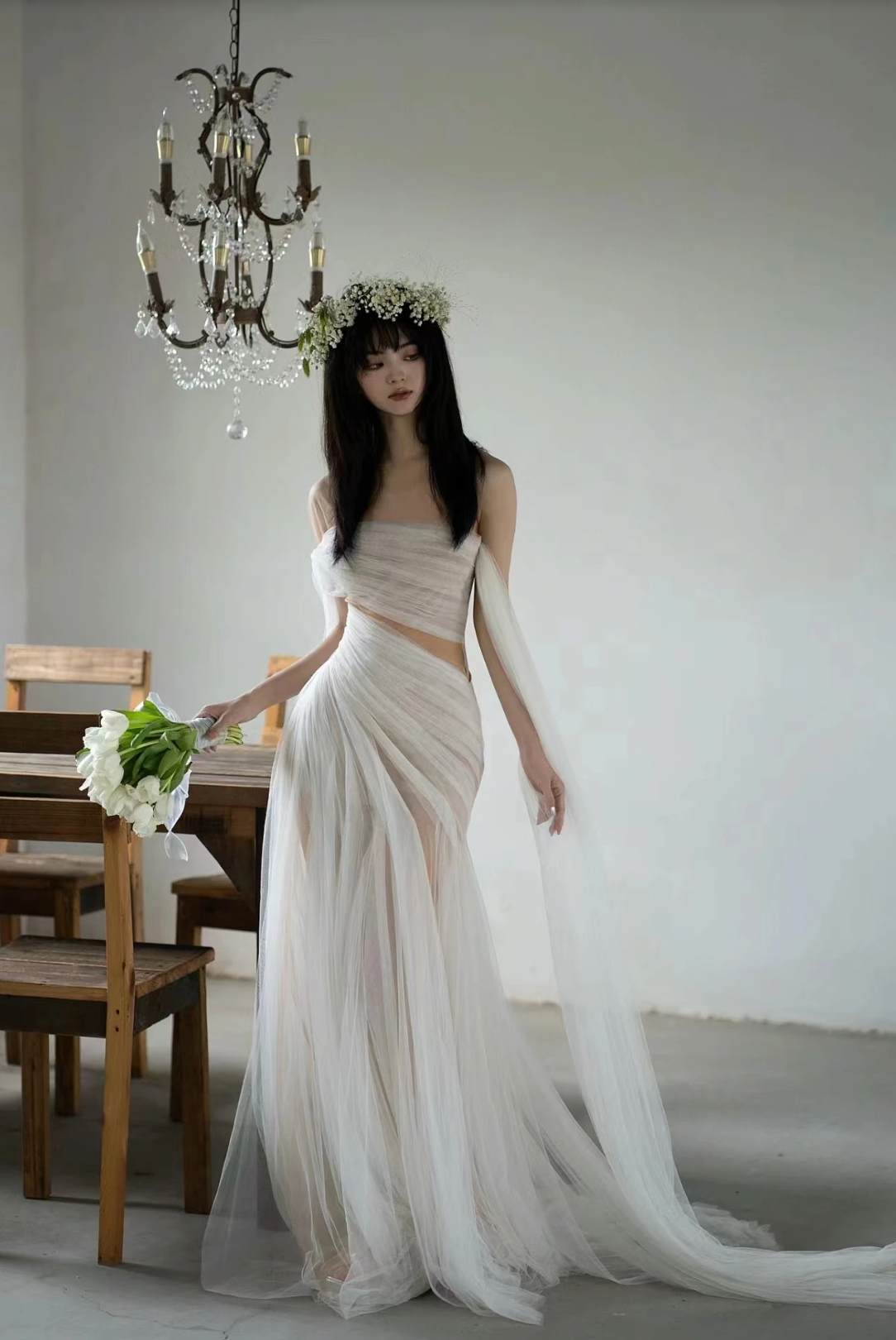 A woman wearing the Old Money Collection La Digue Gown with a sheer neck and pleated tulle, featuring a long ribbon.