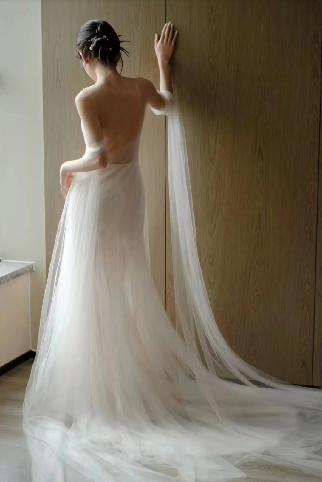 A woman wearing the Old Money Collection La Digue Gown with a sheer neck and pleated tulle, featuring a long ribbon.