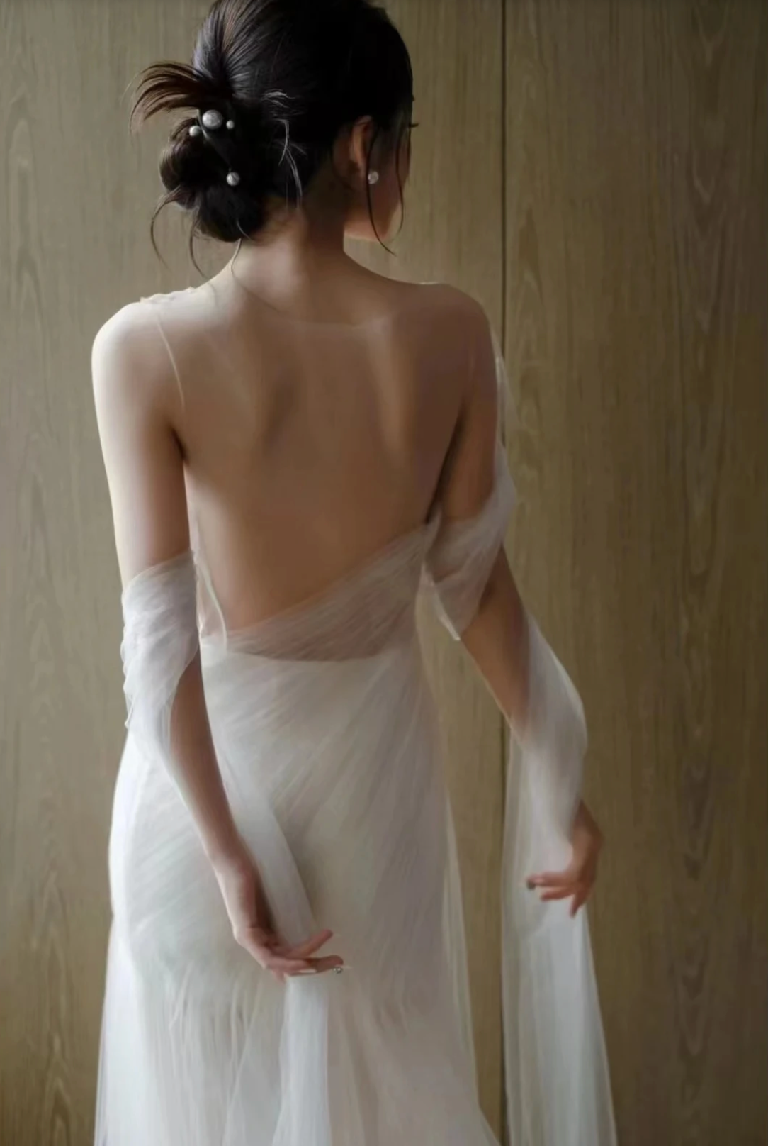 A woman wearing the Old Money Collection La Digue Gown with a sheer neck and pleated tulle, featuring a long ribbon.